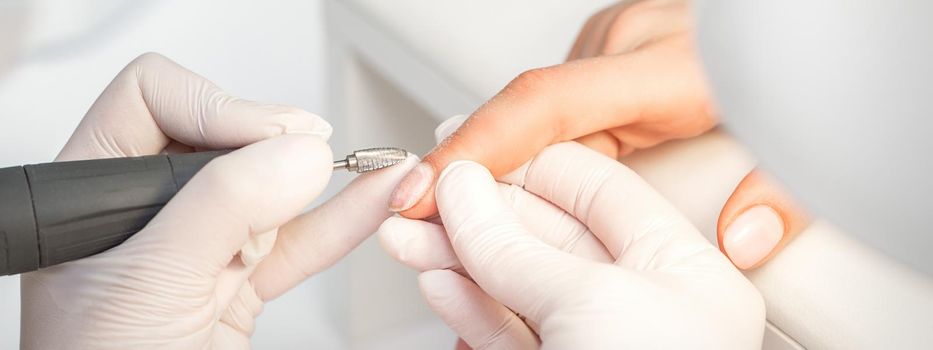 Manicurist removes nail polish uses the electric machine of the nail file during manicure