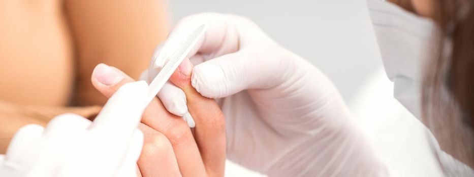 Close up of a manicurist files the female nails with the nail file in a nail salon