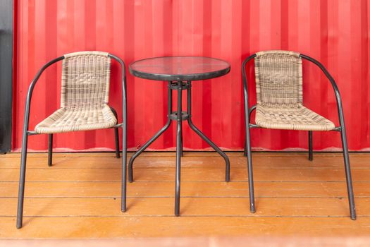 two empty braided chairs and glass table near red wall of roadside cafe at daylight