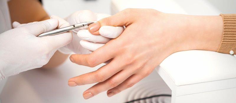 Manicure master is removing cuticles with a nail clipper in a nail salon