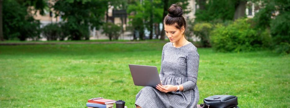 Beautiful young woman sitting on a bench with a laptop and working or studying outdoors