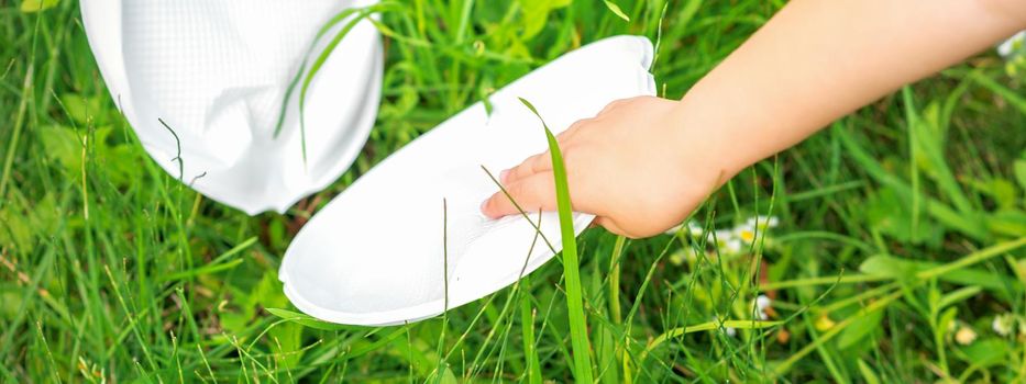 Child's hand cleans park from plastic utensils in the grass in the park