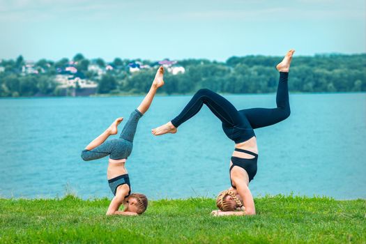 Woman and child doing handstand exercise on the grass near the lake. Yoga nature concept