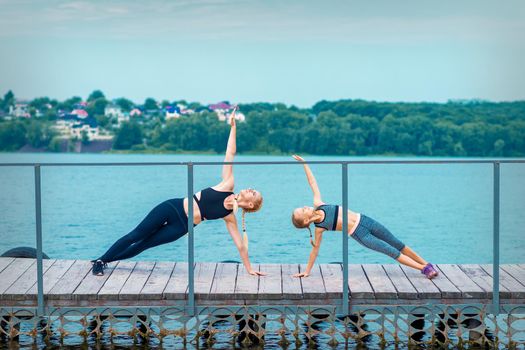 Woman and child are doing sport exercises on hands on the pier the lake