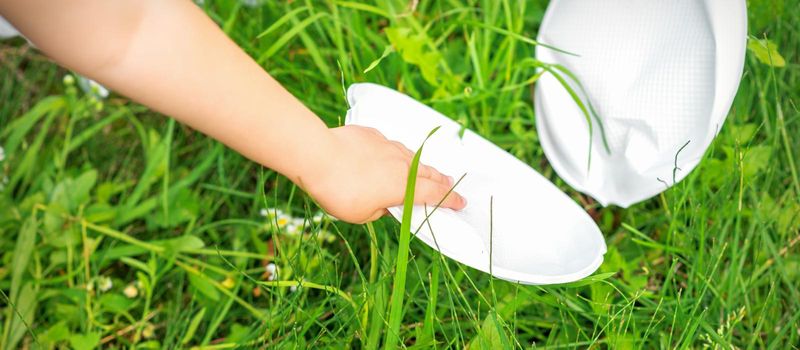 Child's hand cleans park from plastic utensils in the grass in the park