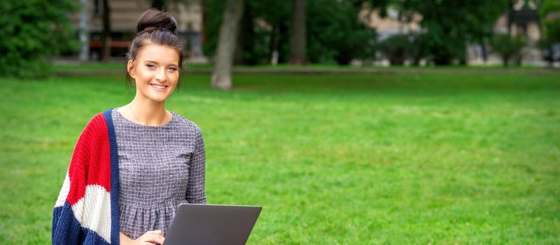 Beautiful happy young woman sitting on the bench with a laptop in the park