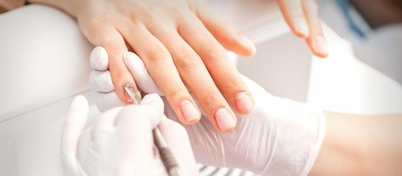 Closeup of beautiful woman's fingernails receiving cleaning cuticle with manicure pusher tool while getting a manicure