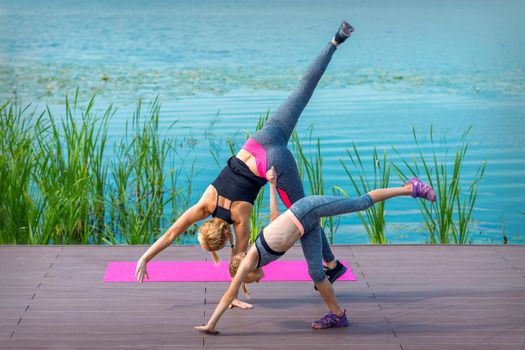 Woman and child doing handstand exercise on the grass near the lake. Yoga nature concept