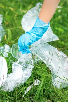 Child's hand cleans park from plastic utensils in the grass in the park