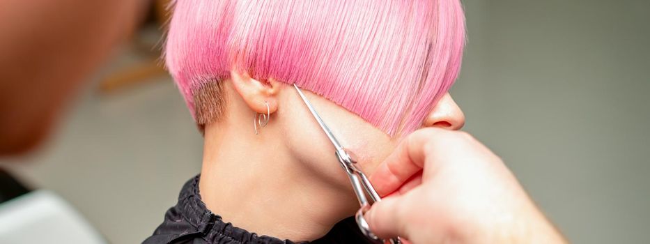 Close up of hairdresser cutting short pink hair of the young woman in a hair salon