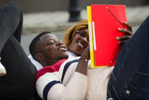 Young students lying on the floor after classes looking at documents laughing.