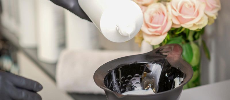 Hairdresser's hand mix hair dye in a black bowl in a beauty salon