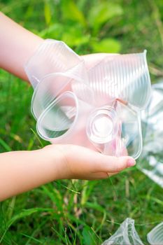 Child's hands clean the park from used plastic utensils in the grass