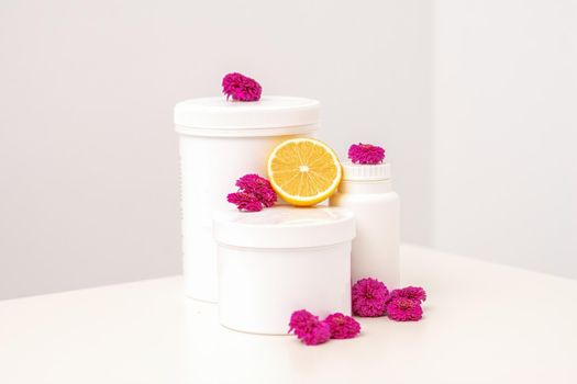 White cosmetic jars, containers, bottle with fresh lemon and chrysanthemums flowers on white background with copy space. Blank space for branding mockup beauty product