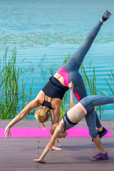 Woman and child doing handstand exercise on the grass near the lake. Yoga nature concept
