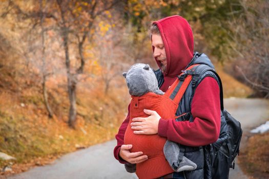 Young father with his baby boy in ergonomic baby carrier in autumn nature. Babywearing and active father concept.