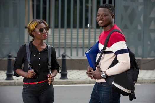 two students, girl and boy with notebooks and backpacks walking and talking in the city. Education concept