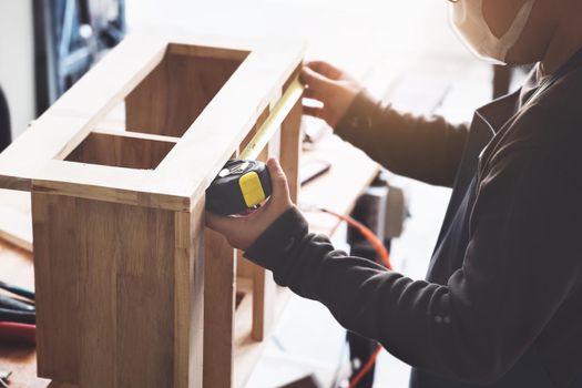 A carpenter measures the planks to assemble the parts and build a wooden table for the customer.