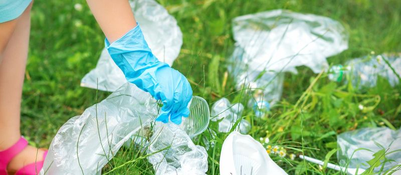 Child's hand cleans park from plastic utensils in the grass in the park