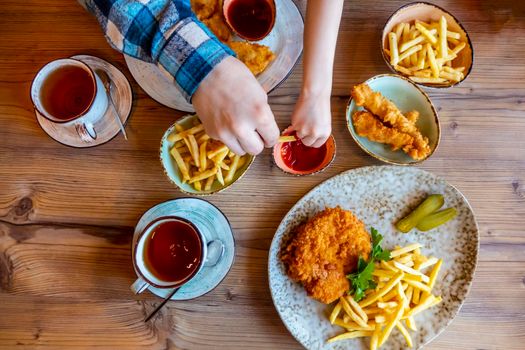 Children and man hands Picking French Fries on wood table in restaurant. French fries with ketchup on wooden background. High quality photo