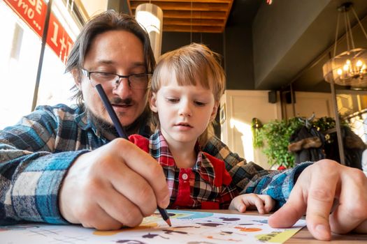 a child with his father in a restaurant draws a coloring book, waiting for cooking