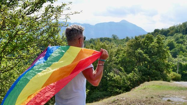 Bisexual, gay, old man, male, transsexual walk back with LGBTQIA flag, rainbow peace in pride mounts on the nature on a day and celebrate Bisexuality Day or National Coming Out Day