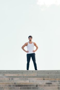 vertical photo of a handsome sportsman standing with his hands on his hips at the top of a staircase, concept of urban sport and healthy lifestyle, copy space for text