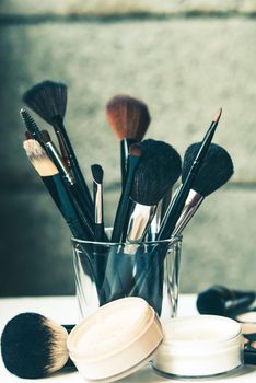 professional brushes in glass in fron of gray wall with powder