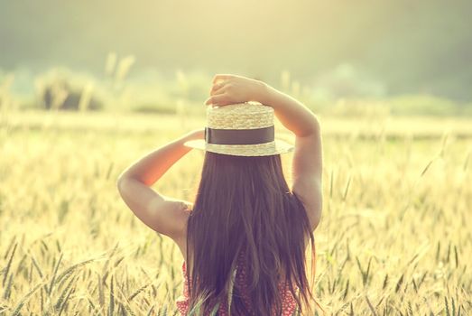 young woman in straw hat in the middle of wheat field enjoing summertime