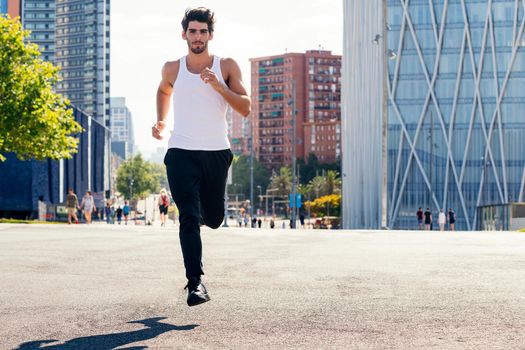 front view of a sporty man running on the asphalt in the city, concept of urban sport and healthy lifestyle, copy space for text