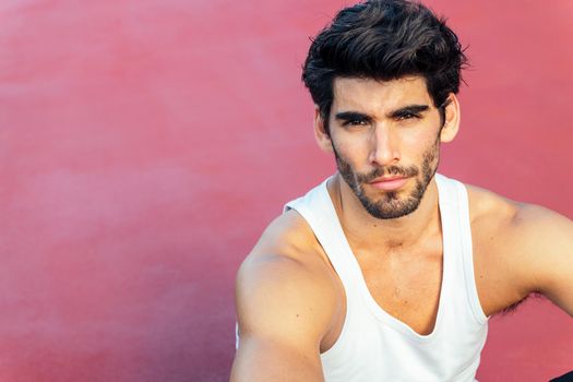 portrait of a handsome sportsman sitting on a red floor, concept of urban sport and healthy lifestyle, copy space for text