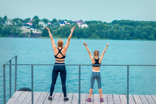Woman and child are doing hands up exercises on the pier the lake