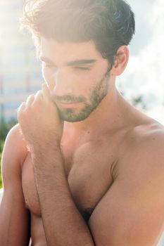 vertical portrait of a handsome shirtless sportsman posing at sunset in front of city buildings, concept of urban sport and healthy lifestyle