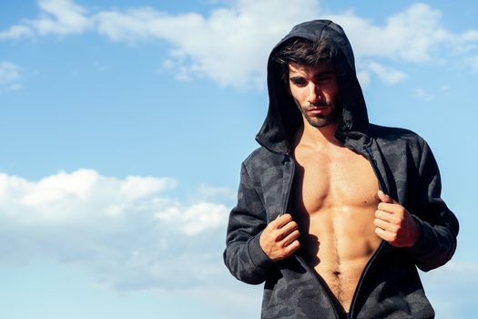 handsome sportsman showing off his muscles under a hooded sweatshirt, concept of sport and healthy lifestyle, copy space for text