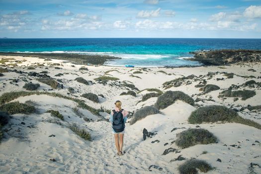 Female tourist visiting white beach of Caleta del Mojon Blanco. Sandy desert beach and rugged coastline. Orzola, Lanzarote, Canary Islands, Spain, Africa