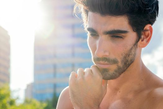 portrait of a handsome shirtless sporty man posing at sunset in front of city buildings, concept of urban sport and healthy lifestyle, copy space for text