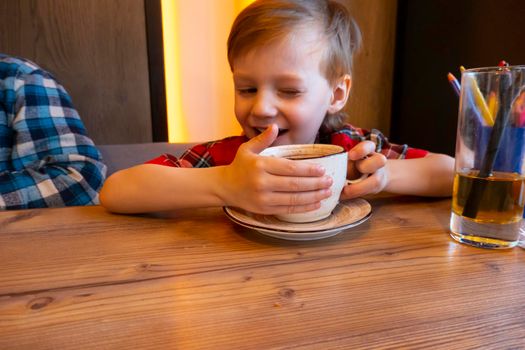 Little boy drinking from a cup tea in a cafe. High quality photo