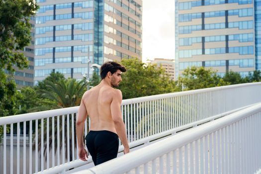 sportsman walking shirtless on a city bridge in front of buildings, concept of urban sport and healthy lifestyle