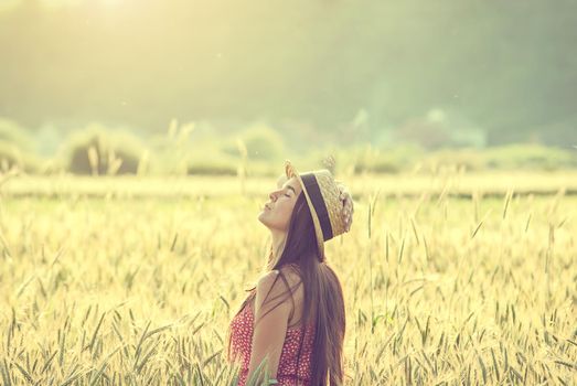 young woman in straw hat in the middle of wheat field enjoing summertime