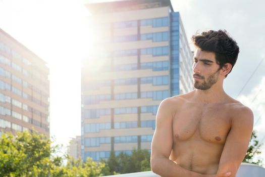 handsome shirtless sportsman posing at sunshine in front of city buildings, concept of urban sport and healthy lifestyle, copy space for text