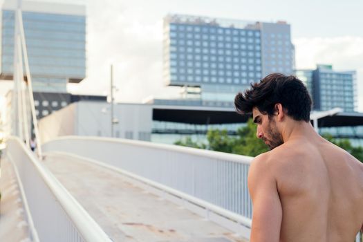 shirtless athlete concentrating next to a city bridge in front of buildings, urban sport and healthy lifestyle concept, copy space for text
