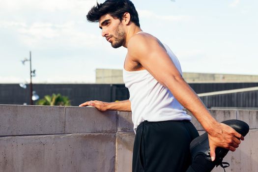 handsome sportsman stretching his leg muscles on a concrete wall, concept of urban sport and healthy lifestyle