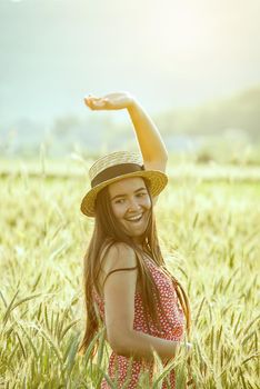 young woman in straw hat in the middle of wheat field enjoing summertime