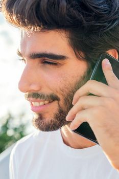 portrait of a handsome young man smiling and talking on his phone at sunset, concept of technology and urban lifestyle, copy space for text