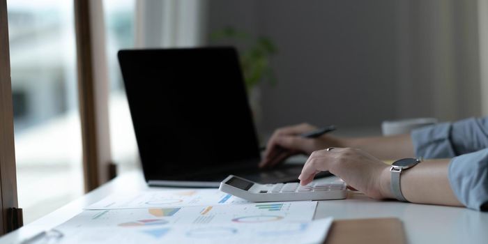 Close up Business woman using calculator and laptop for do math finance on wooden desk in office and business working background, tax, accounting, statistics and analytic research concept.