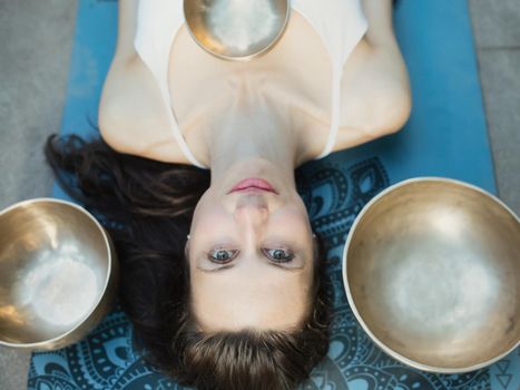 Yoga concept, meditation and sound therapy. Portrait of beautiful young caucasian woman surrounded by copper tibetan singing bowls and instruments.