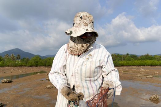 Ko Phangan, Thailand, March 15, 2022: fully covered old woman looking for clams on the beach