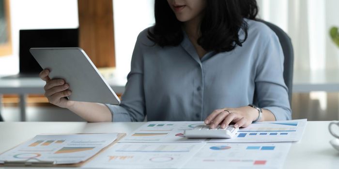 Close up Business woman using calculator and laptop for do math finance on wooden desk in office and business working background, tax, accounting, statistics and analytic research concept.