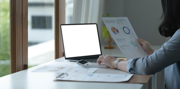 Close up Business woman using calculator and laptop for do math finance on wooden desk in office and business working background, tax, accounting, statistics and analytic research concept.