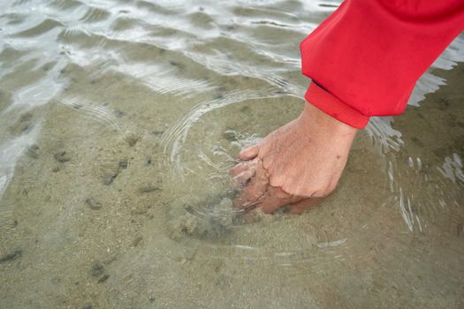 Ko Phangan, Thailand, March 15, 2022: woman's hand picking up a clam from the sand of the sea